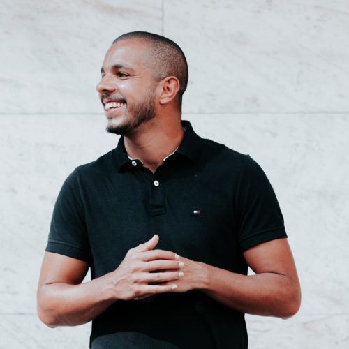 man in black polo shirt standing near white wall